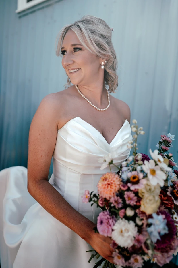 Real bride in strapless satin wedding dress with draped bodice, pearl necklace, & colourful bouquet, in Auckland, New Zealand.