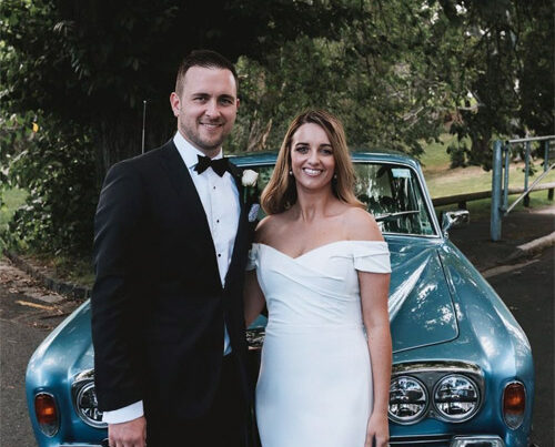 Bride and groom standing with wedding car.