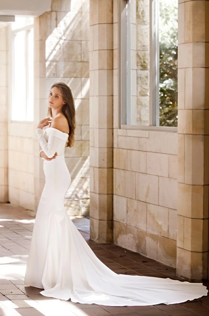 Ivory off-the-shoulder wedding dress with fitted silhouette, soft train and long sleeves, designed by Anna Schimmel in Auckland.