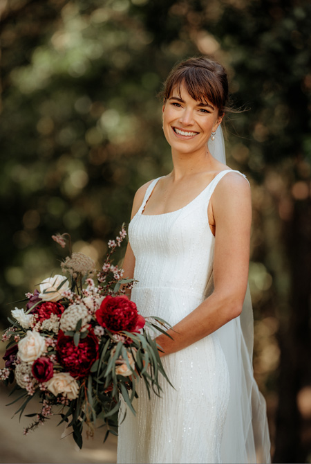 Real bride wearing simple wedding dress, holding bouquet.