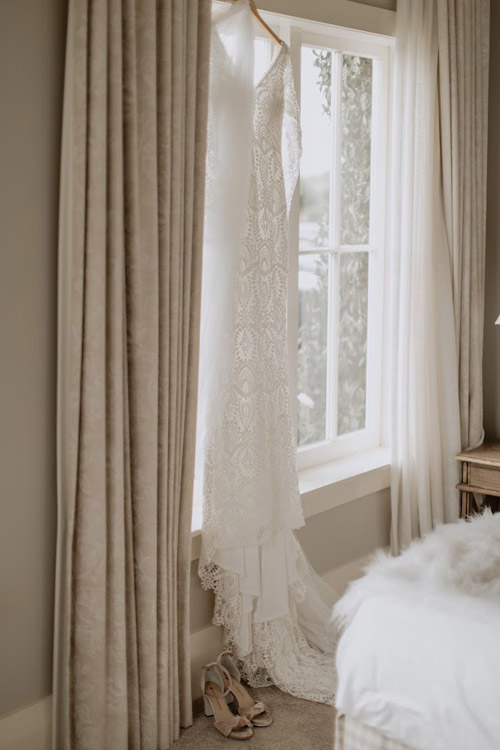 Vintage lace wedding dress, hanging by window.