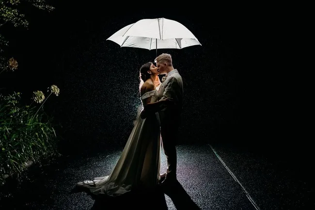 Bride and groom kissing under umbrella in the rain.