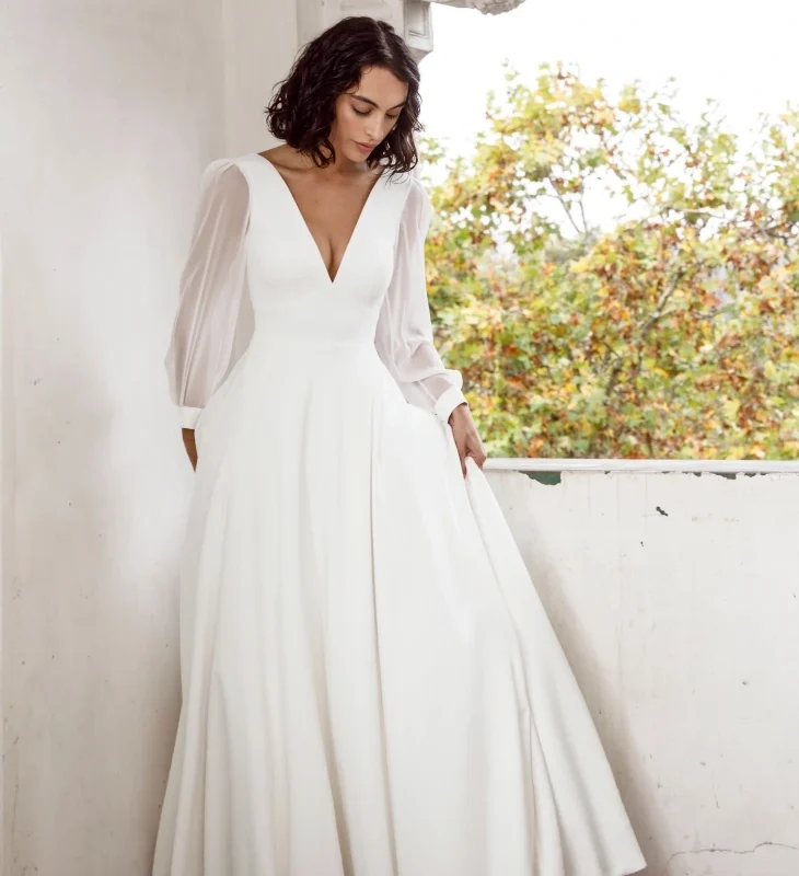 Ivory elegant wedding dress in matte crepe with a deep V-neckline, sheer chiffon sleeves, buttoned cuffs and flowing A-line skirt.