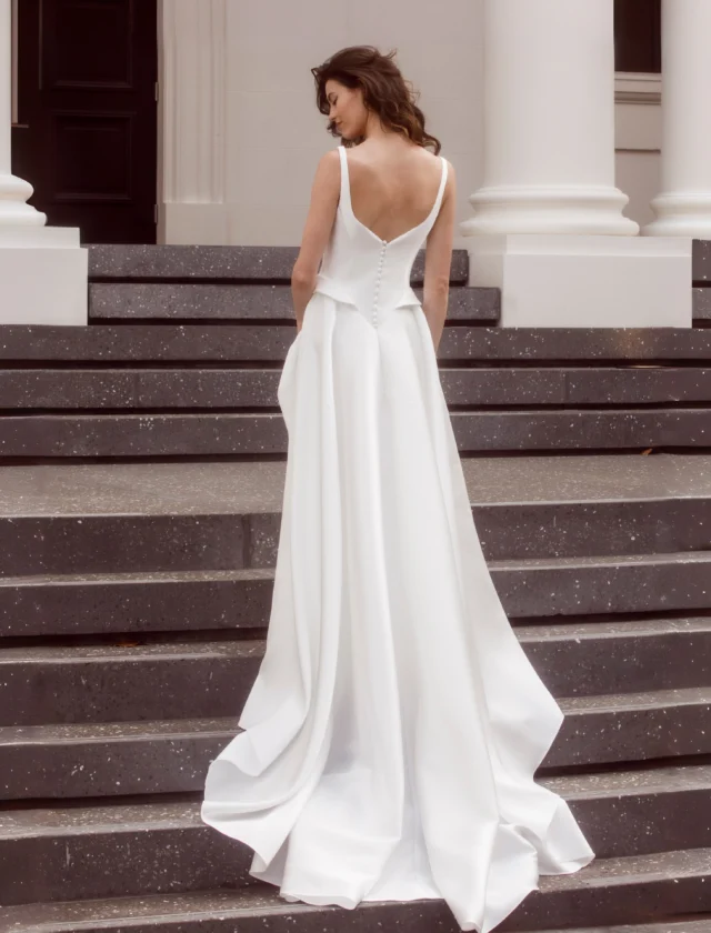 Can a simple wedding dress still make an entrance?

Absolutely. Sometimes the fabric and the cut do all the work.

Laura is cut in glossy Mikado satin, with a beautifully structured bodice and a stepped basque waist that defines the shape before opening into a full A-line skirt.

Turn around and the details really come into their own - a low V-back, slender straps, tiny covered buttons and that subtle peplum shaping over the hip.

No lace. No beading. No embellishment needed.

Just beautiful satin, strong lines and a silhouette that looks quite spectacular in movement.

For the bride who wants simple, but definitely not plain.

Laura is available to try at our Auckland bridal boutique by appointment.

#SatinWeddingDress #MikadoWeddingDress #BasqueWaistWeddingDress #nzbridal